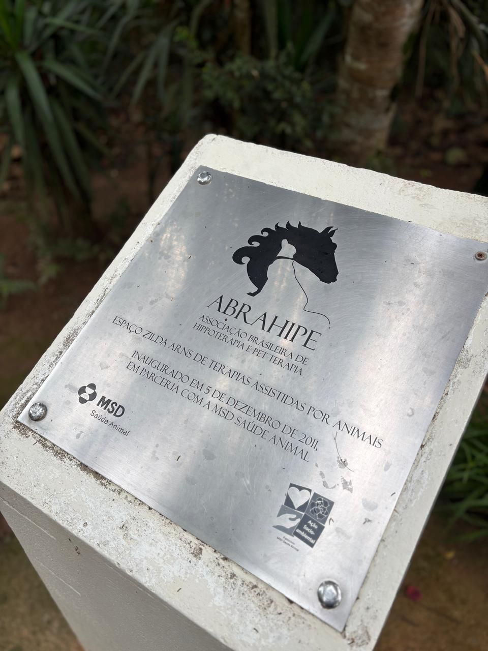 Placa de metal com a logo da ABRAHIPE e a marca da MSD.