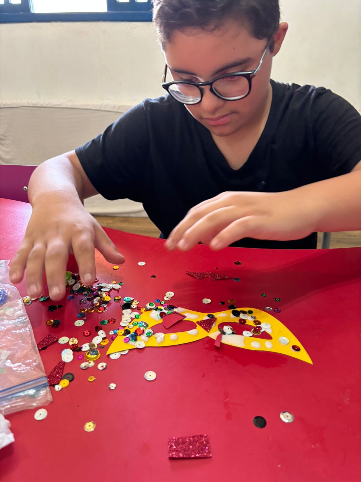 Menino de óculos fazendo uma colagem com papel picado na oficina de artes.