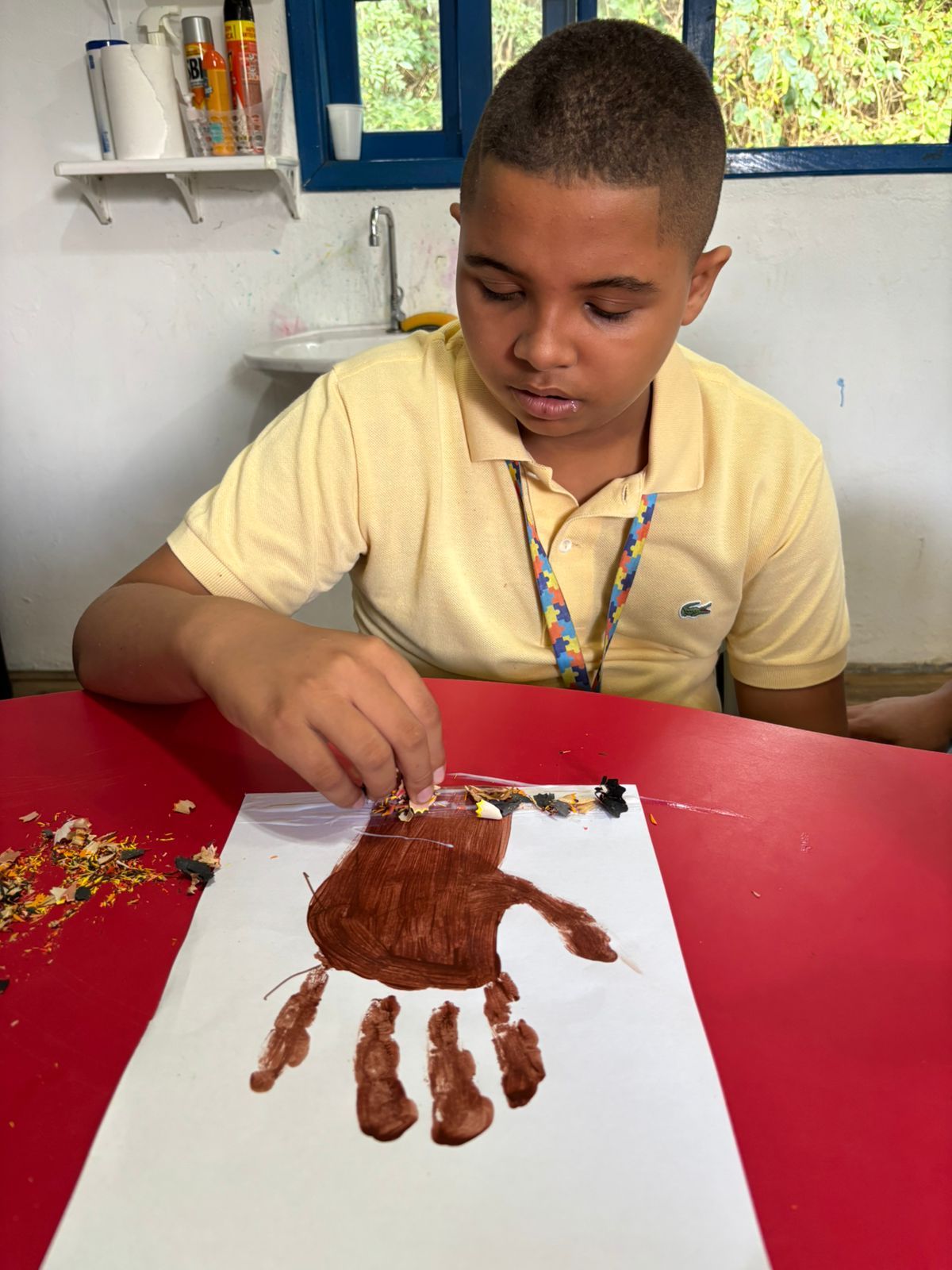 Menino carimbando a mão com tinta marrom numa folha branca.