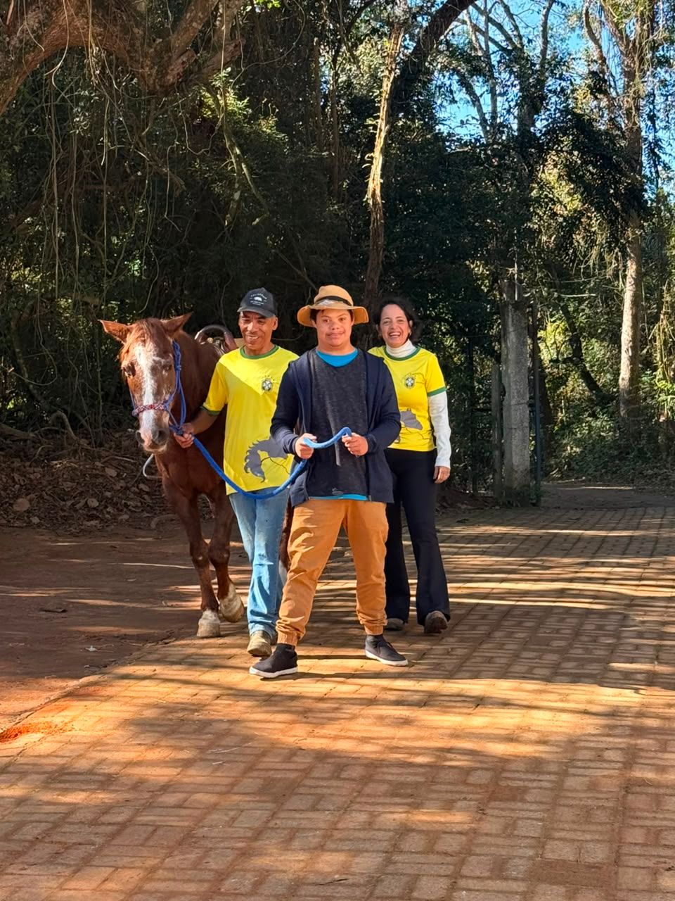 Atendido caminhando com dois profissionais e um cavalo numa trilha no fim da tarde.