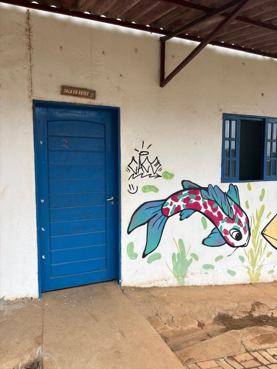 Porta azul de uma sala, com um peixe colorido pintado na parede.