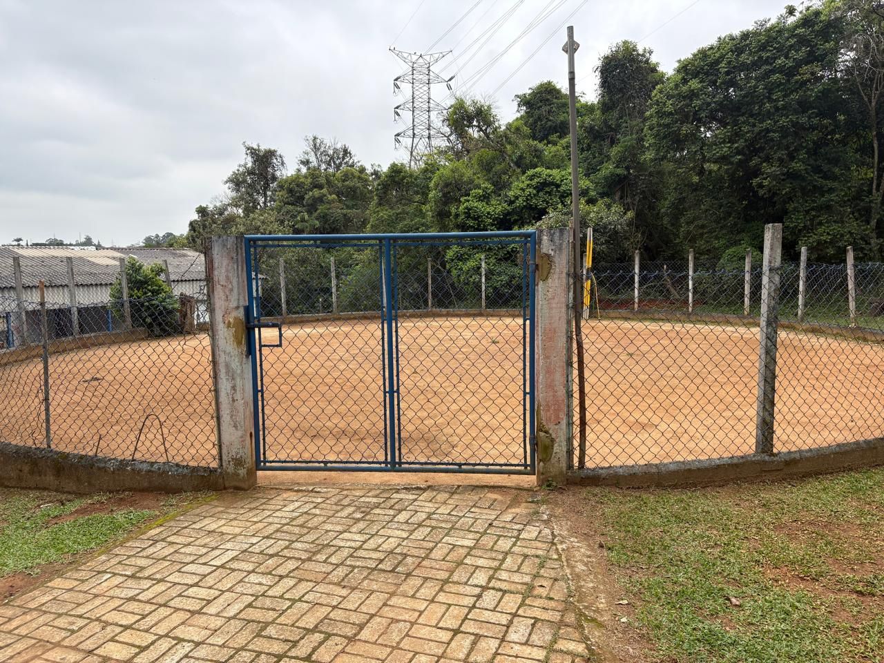Redondel cercado, com portão azul, ao lado da mata.