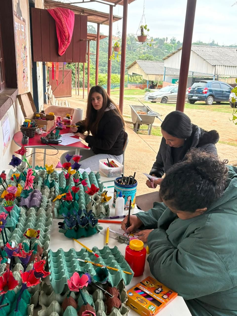 Familiares fazendo flores de caixa de ovo numa oficina na varanda.